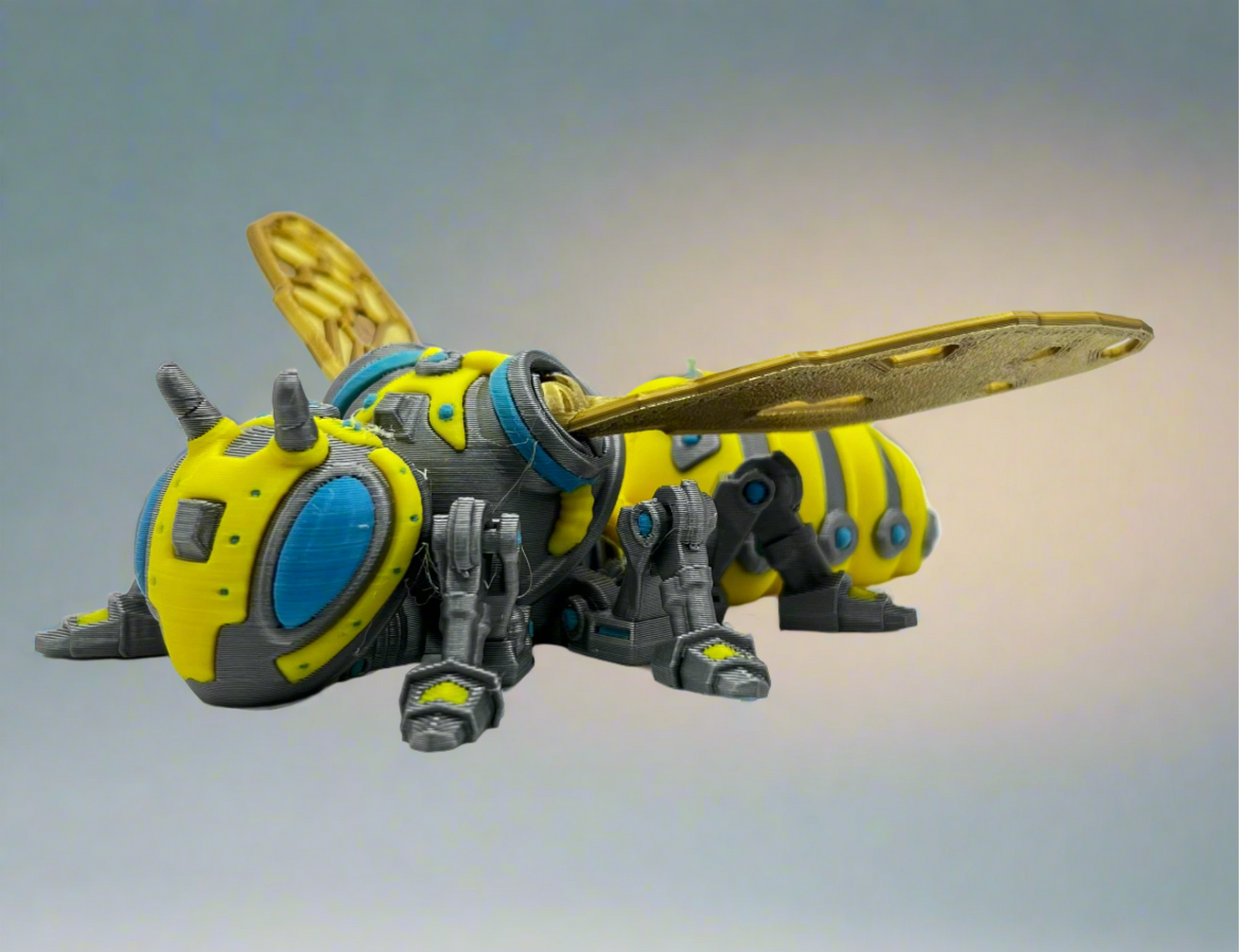 Front view of the 3D-printed RoboBee model, showcasing its intricate robotic design and vibrant yellow, blue, and metallic gray colors.